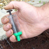A hand holding a Magic Seeder, a flower seeder for sowing seeds, with a clear body and green accents.