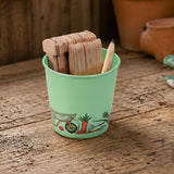 Mint Green tin on a table with plant labels and a pencil, set on a rustic wooden table.