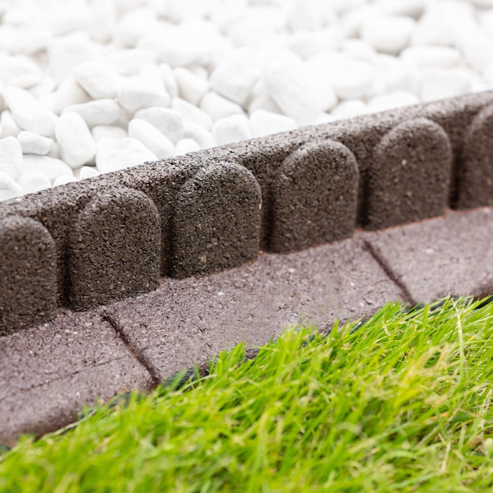 Close-up of green lawn edging made from recycled tyres, installed on a lawn with a mower in the background.