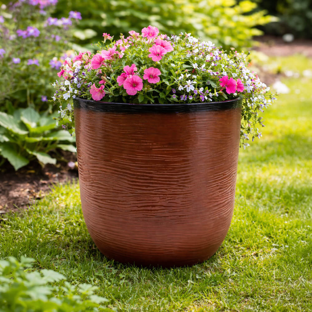 Brown planter with pink and white flowers on a grassy lawn