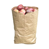A beige paper sack filled with potatoes, placed against a stone wall.