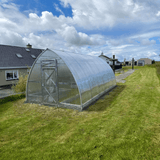 Greenhouse on a grassy area with houses and cloudy sky in the background