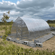 Partial construction of a greenhouse with transparent plastic covering in an outdoor setting.