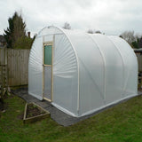 Polycarbonate greenhouse with a wooden door on grass