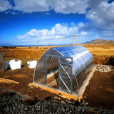 Metal greenhouse in a rural setting with a blue sky and clouds.
