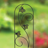 A black metal plant pot trellis with yellow accents and bee silhouettes on it, standing upright in a garden setting.