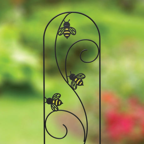 A black metal plant pot trellis with yellow accents and bee silhouettes on it, standing upright in a garden setting.