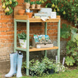 Green and wooden potting table covered in potting products in garden