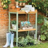 Green and wooden potting table covered in potting products in garden