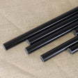 A collection of black powder coated fruit cage aluminium poles of various lengths laid out on a textured fabric surface.