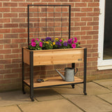 Wooden planter with flowers and a watering can on a brick wall background