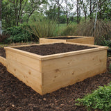 Two wooden raised garden beds in a natural setting with trees and shrubs.