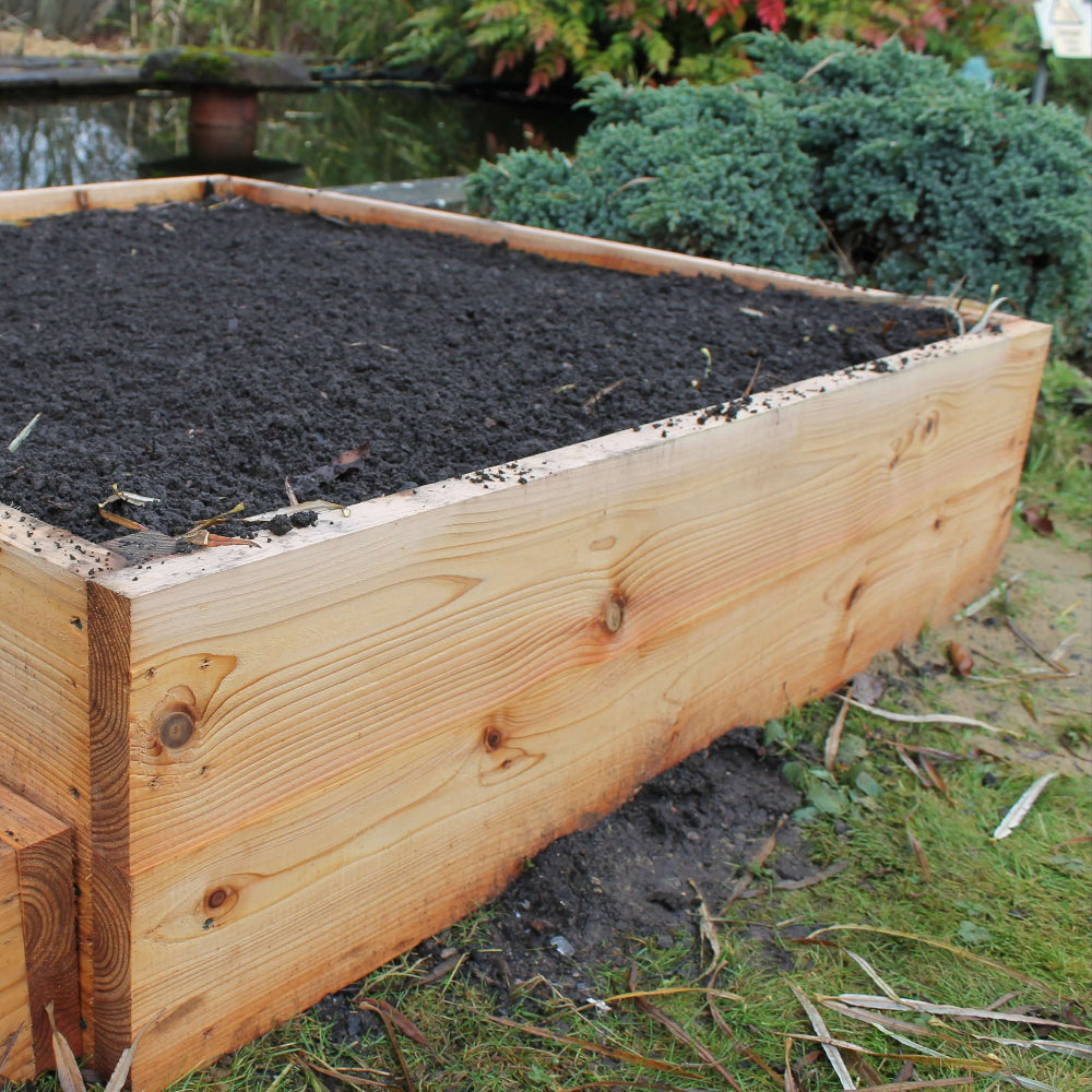 Wooden raised garden bed with soil in a garden setting
