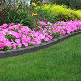A grey, rubber garden border strip installed around a bed of pink flowers on a lawn.