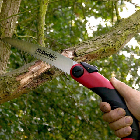 A person is using a red and black Sabre Tooth folding saw to cut a branch