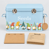 A light blue metal seed storage box with a gnome-themed border and the word 'Seeds' printed on the front, shown with kraft paper seed cards on a white background.