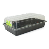 A black plastic seed tray with drainage holes, placed on a wooden surface with a plant in the background.