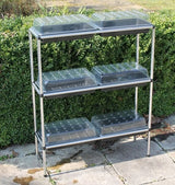 A three-tiered seed tray stand stood in a garden with propagators on