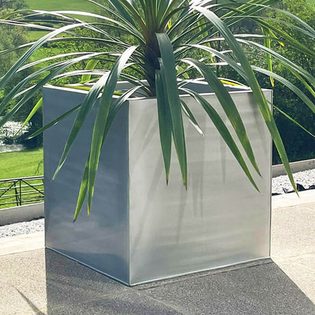 Cube silver planter in a garden with plant in it