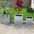 Three silver cube-shaped zinc planters in different sizes, with the smallest in front, medium in the middle, and largest in the back, placed on a patio with plants inside them.