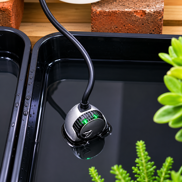 A black smart valve installed in a green plant watering system, with a cable connected to it.