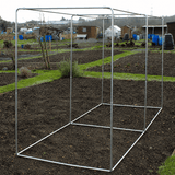 square vegetable cage on a garden bed with a background of greenery and buildings.