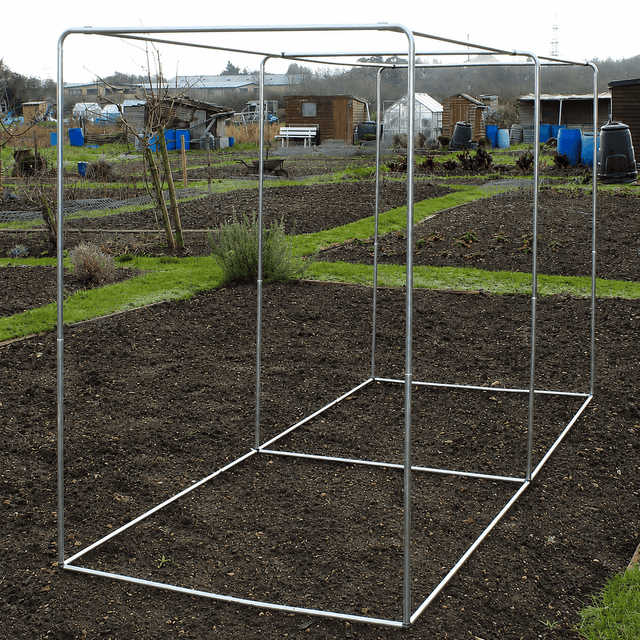 square vegetable cage on a garden bed with a background of greenery and buildings.