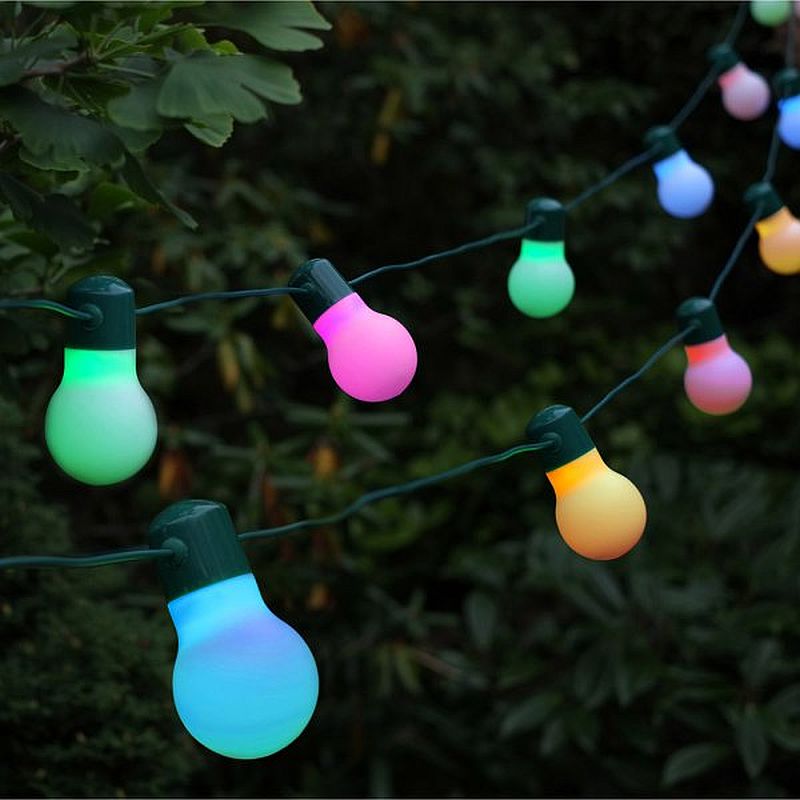 A string of multicolored solar-powered party lights glowing in the dark, attached to a greenery backdrop.