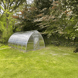 Polycarbonate greenhouse in a garden setting with trees and grass.