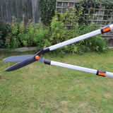 Telescopic grass pruner on grass with plants and wooden fence in the background