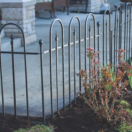 A black, metal triple arch fence panel kit installed around a garden bed with a pathway in the background.
