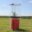 A clear plastic tomato cloche twist-up design standing on a grassy field, covering a plant inside.