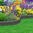 A curved brick patterned lawn edging installed around a bed of colorful flowers and green grass.