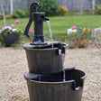 Solar Barrel and Pump Water Feature displayed in colourful garden filled with greenery and flowers.