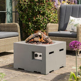 A grey square fire pit on a patio, surrounded by chairs and a table