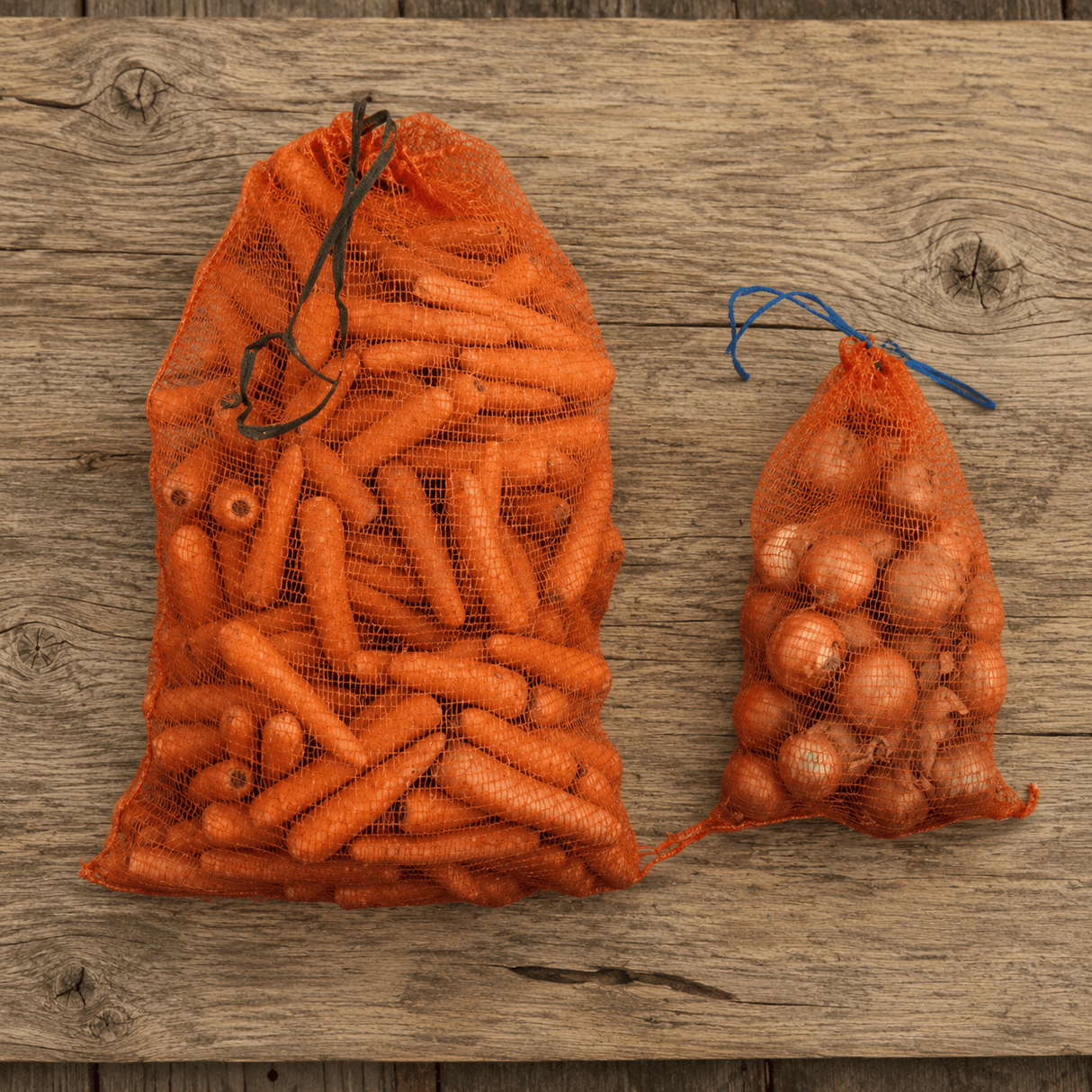 Two mesh bags filled with carrots and potatoes on a wooden surface