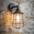 An outdoor wall-mounted light fixture with a charcoal matt finish and a glass cage, mounted on a brick wall.