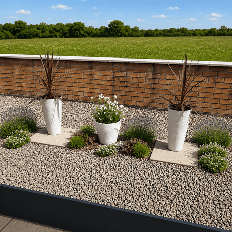 slim white flower pots on gravel surface with a brick wall and green field in the background