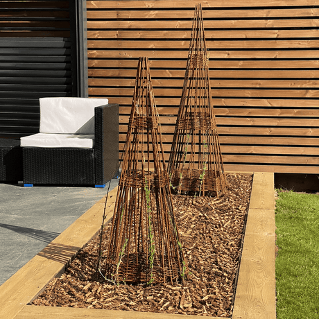Two decorative trellises in a garden bed with a wooden fence and outdoor furniture in the background.