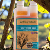 A 500ml bottle of gardening-naturally Winter Tree Wash standing outdoors on tree branches with blurred green leaves and sunlight in the background.