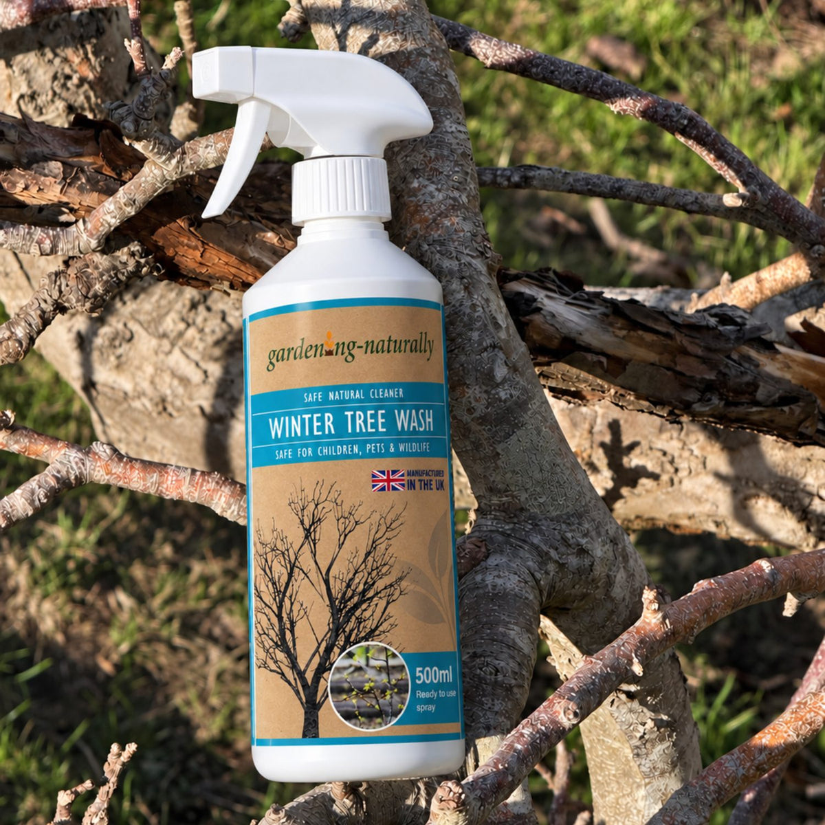 A 500ml spray bottle of Gardening Naturally Winter Tree Wash, designed for cleaning dog and cat urine, shown standing upright on tree branches in an outdoor garden setting.