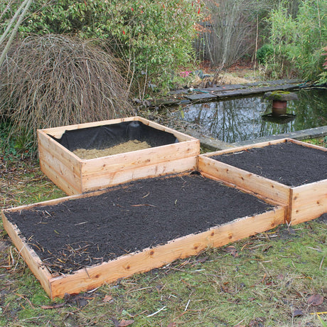 Three wooden raised garden beds with black soil in a garden setting.