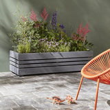 Gray wooden planter with flowers on a stone patio with an orange chair and dinosaur toys.