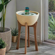 Small indoor fountain on a wooden stand with plants around